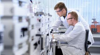 Side angle view of two scientists in a lab at a desk, analysing what’s in front of them